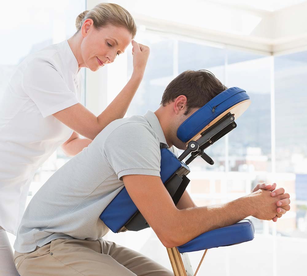 A smiling LoDo massage therapist working on the shoulder of a woman resting peacefully in a massage chair