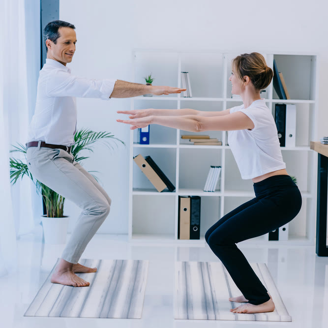 Corporate yoga in Austin: two colleagues in work clothes holding chair pose on yoga mats in an office