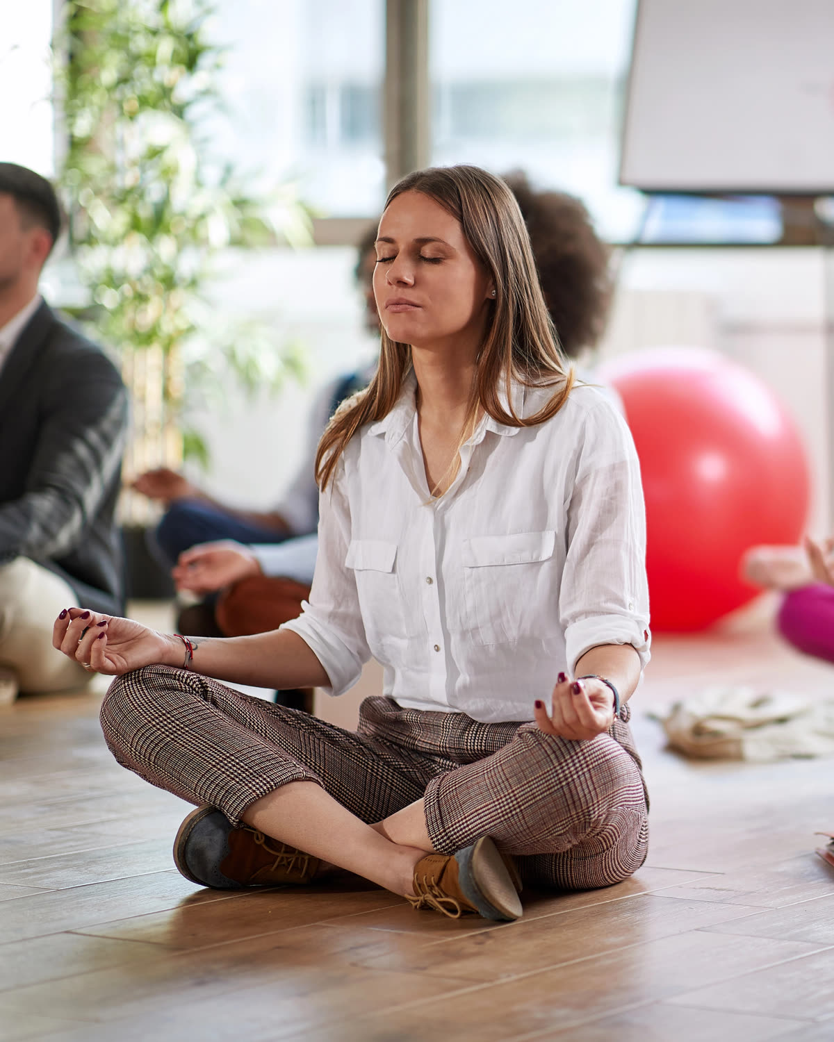 Office meditation in Austin: a woman in work clothes seated cross-legged with her eyes closed among colleagues